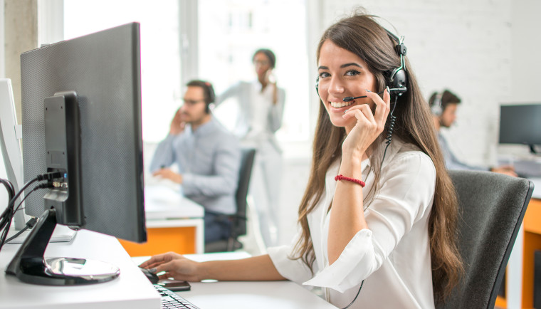 Junge lächelnde Dame bei der Arbeit im Call Center
